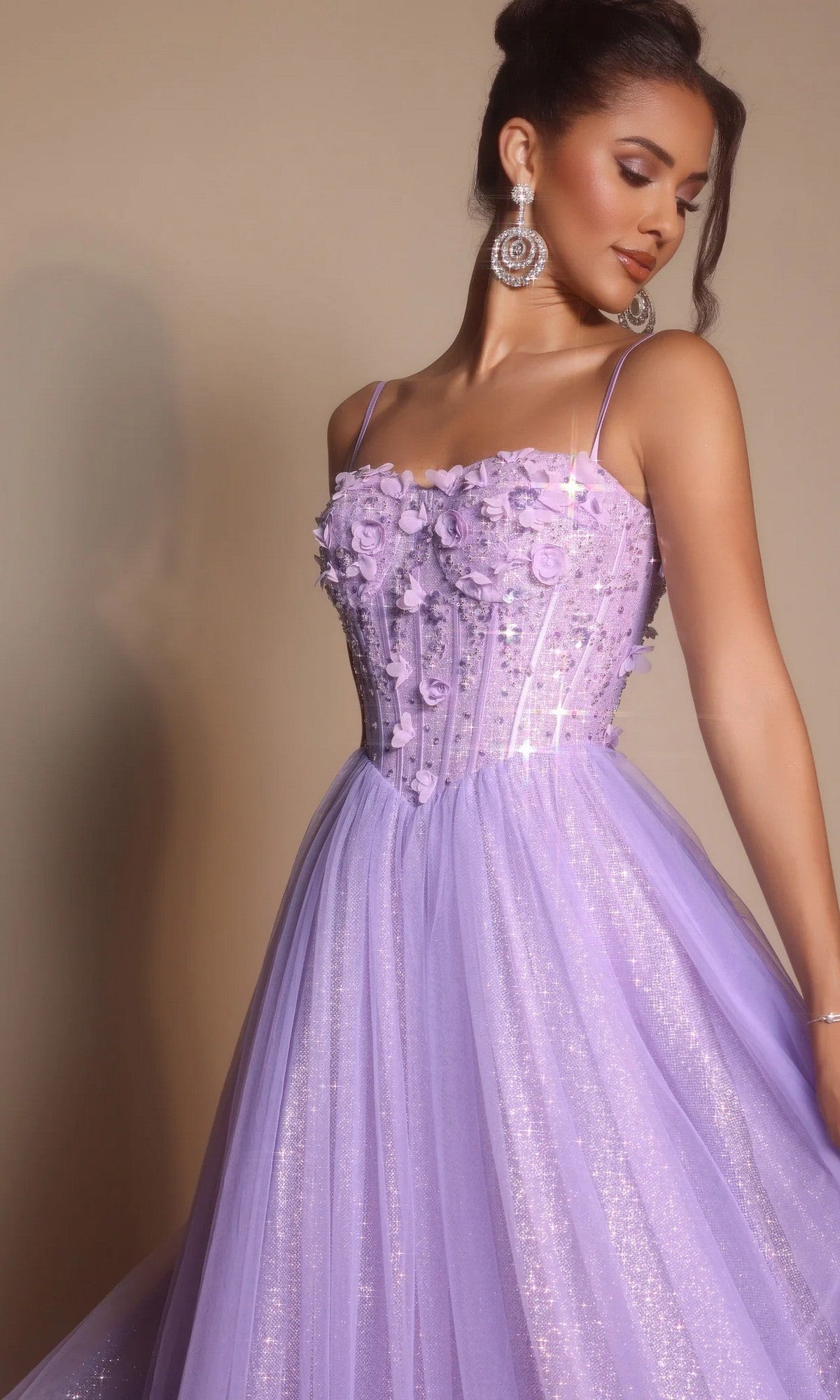 A woman poses against a plain background in the Portia and Scarlett PS26146 Glitter Prom Ball Gown—lavender tulle with glitter, floral appliqué, a boned corset bodice, and delicate spaghetti straps.